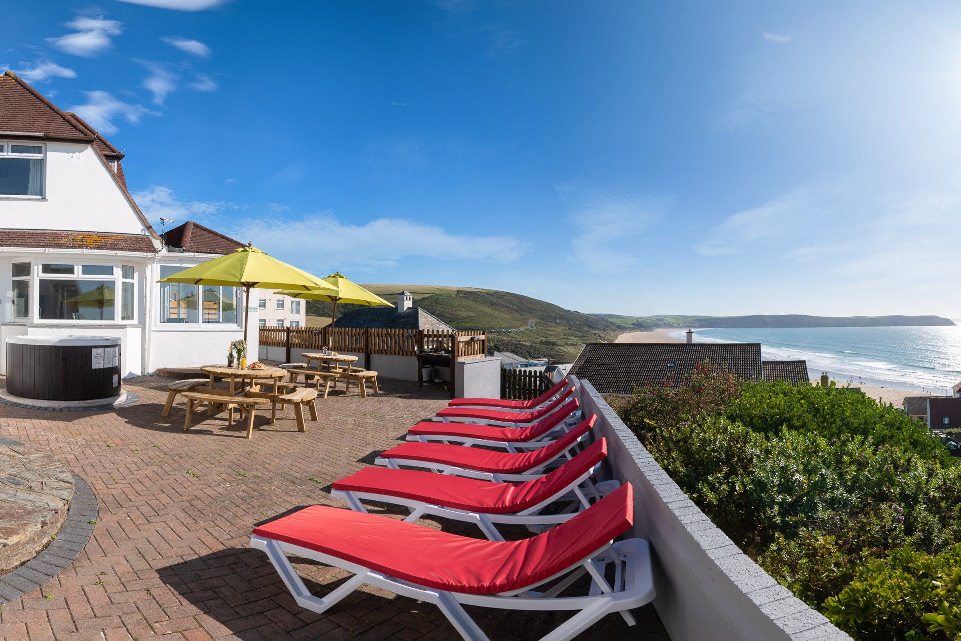A seaside patio with lounge chairs, a hot tub, and a view of the ocean.
