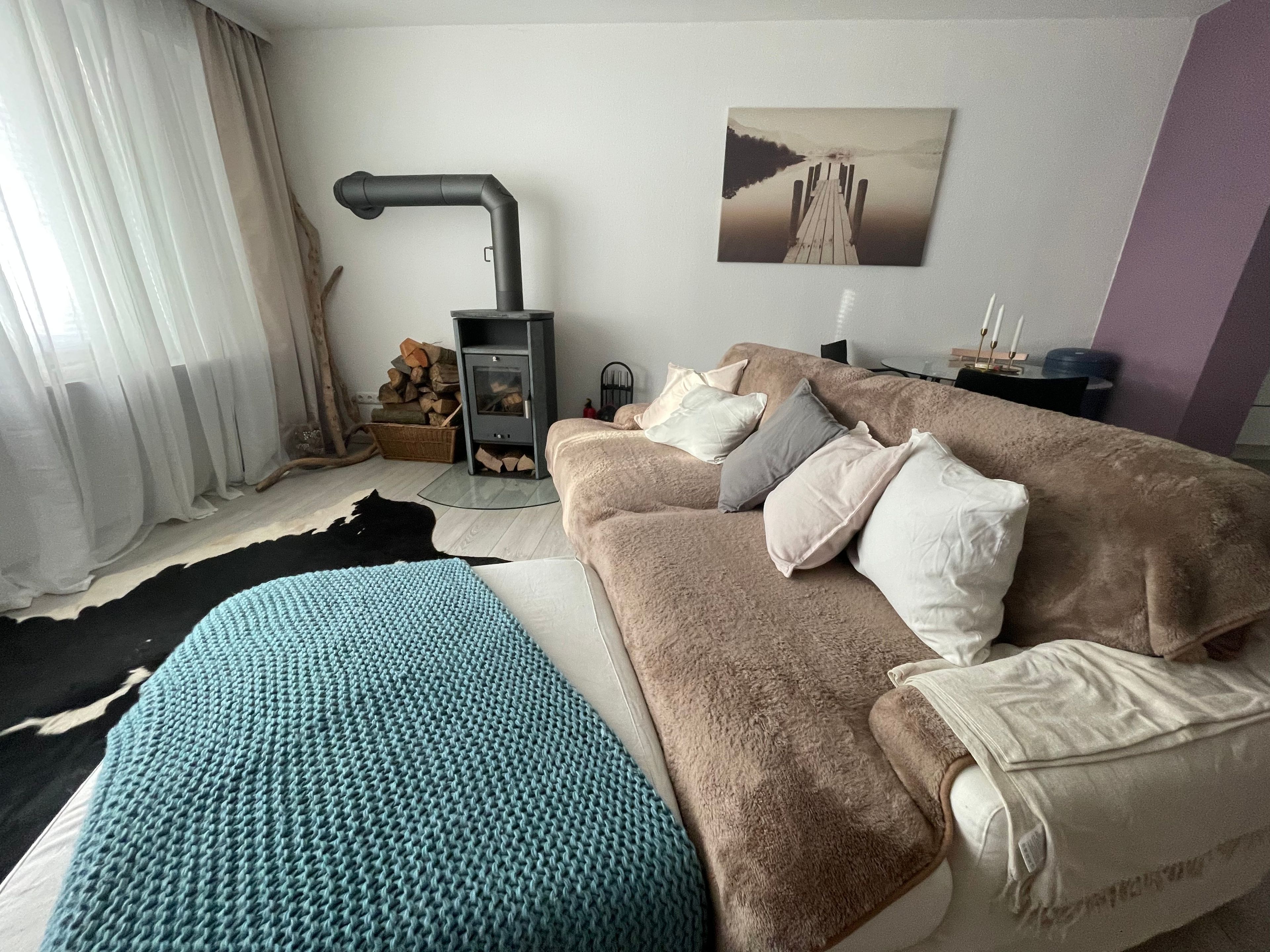 Ein gemütliches Wohnzimmer mit Sofa, Kissen, Teppich, Kamin und einem Bild an der Wand.