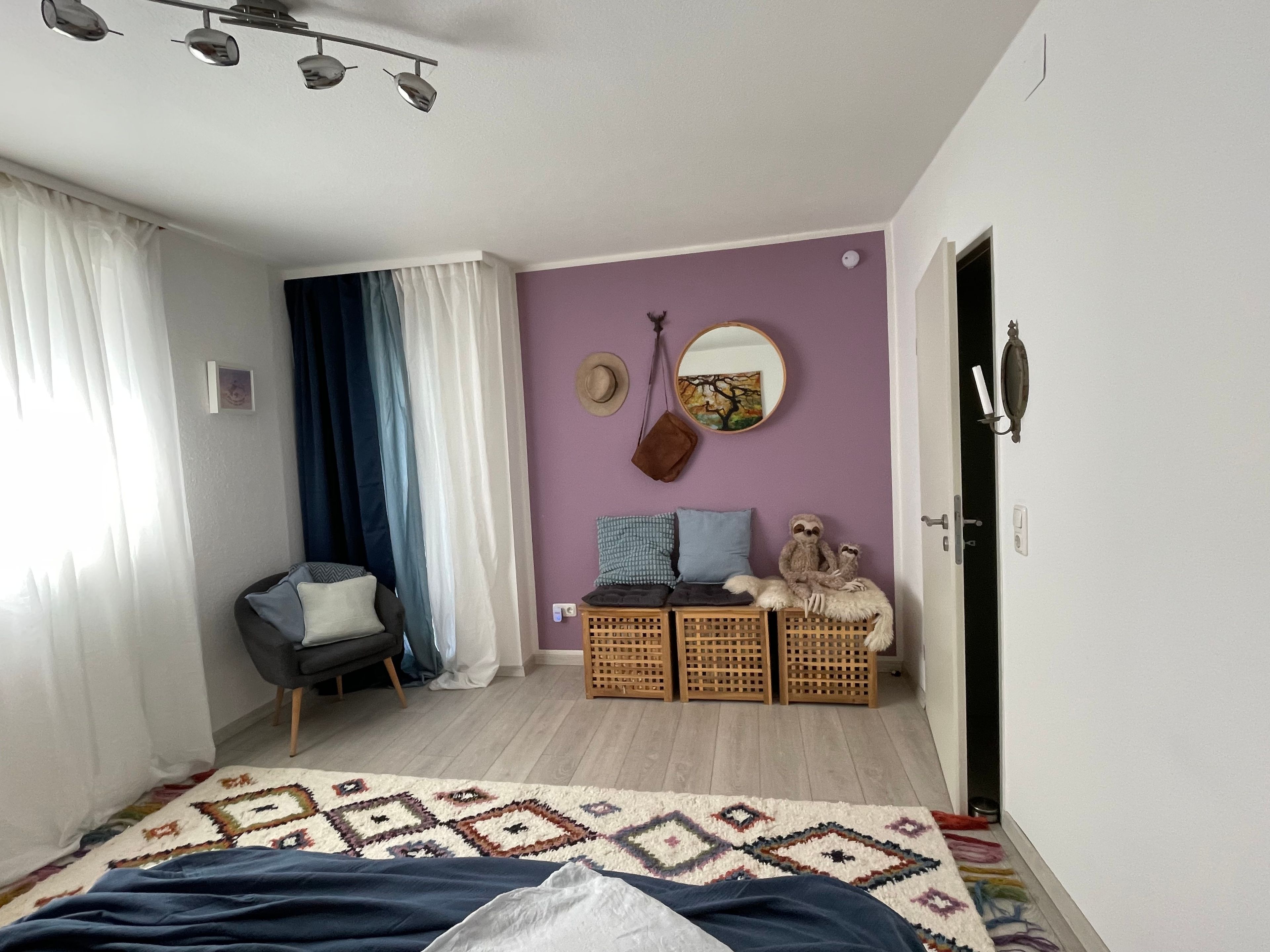 Ein Schlafzimmer mit Bett, Stuhl, Kommode, Spiegel und Tür.
