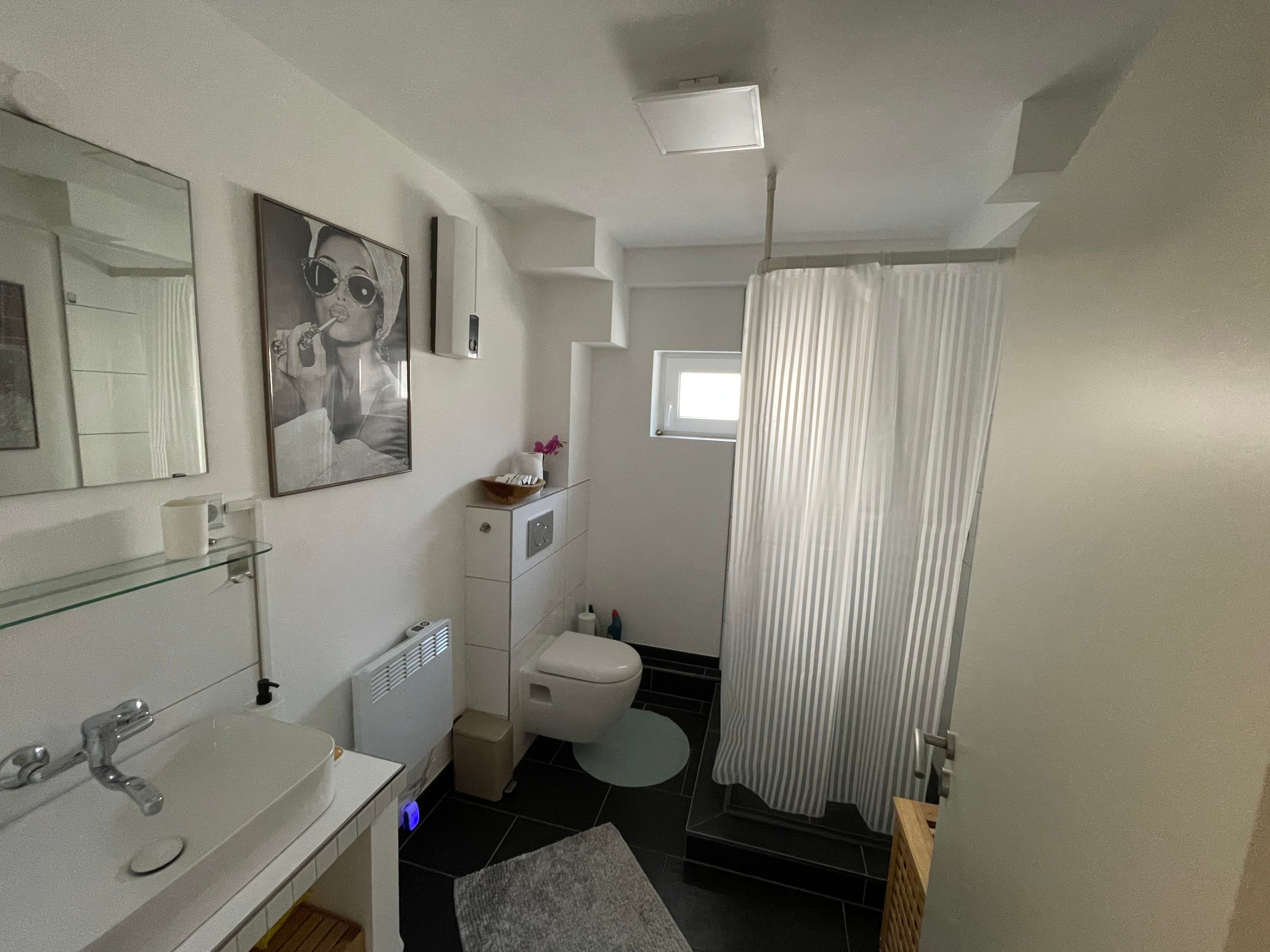 Ein modernes Badezimmer mit einer Glasablage, einer Toilette, einer Duschvorhang und einem kleinen Fenster.