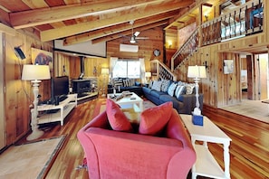 Ein gemütliches Blockhaus-Interieur mit Holzbalkendecke, Kamin, einer Couch und einer Treppe.