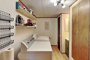 Une buanderie équipée d’un lave-linge, d’un étendoir, d’étagères remplies de divers objets et d’une affiche motivante accrochée au mur.