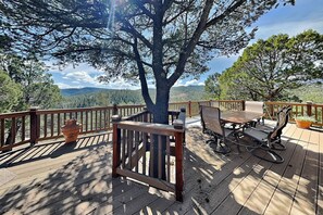 Une terrasse dotée de mobilier d’extérieur, d’un grand arbre et offrant une vue sur un paysage montagneux.