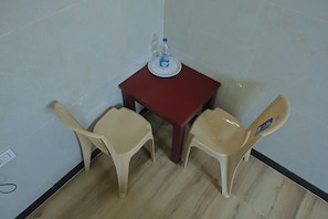 Une petite pièce avec une table rouge et deux chaises beiges. Une bouteille d’eau est posée sur la table.