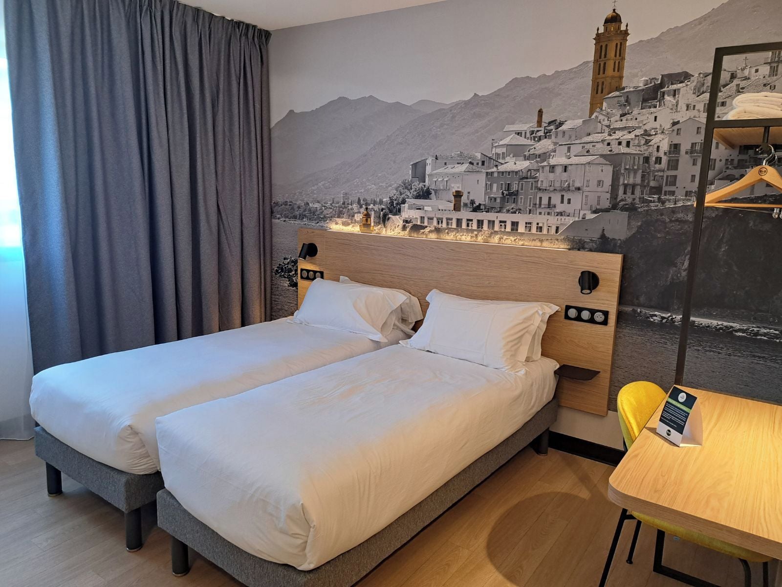 Ein Hotelzimmer mit zwei Betten, einem hölzernen Kopfteil, einem Wandgemälde, einem Tisch und einem Stuhl.