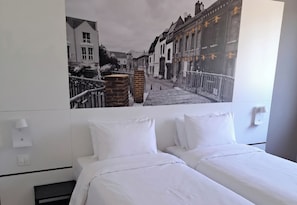 Una habitación de hotel con una cama, una lámpara de pared y un ventanal grande.