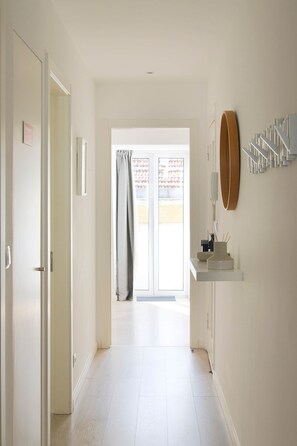A hallway with a door leading to a balcony, a white-framed mirror, and a white shelf with a telephone and a small object. - NEW! Rooftop Charm Lisbon Retreat (Lisbon)