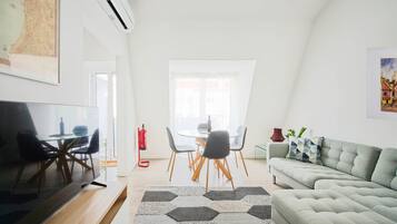 A modern living room with a flat-screen TV, a grey sofa, and a dining area with a glass table and chairs.