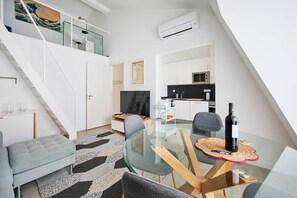 Een modern appartement met een glazen eettafel, een bank, een keuken met een magnetron en een trap.