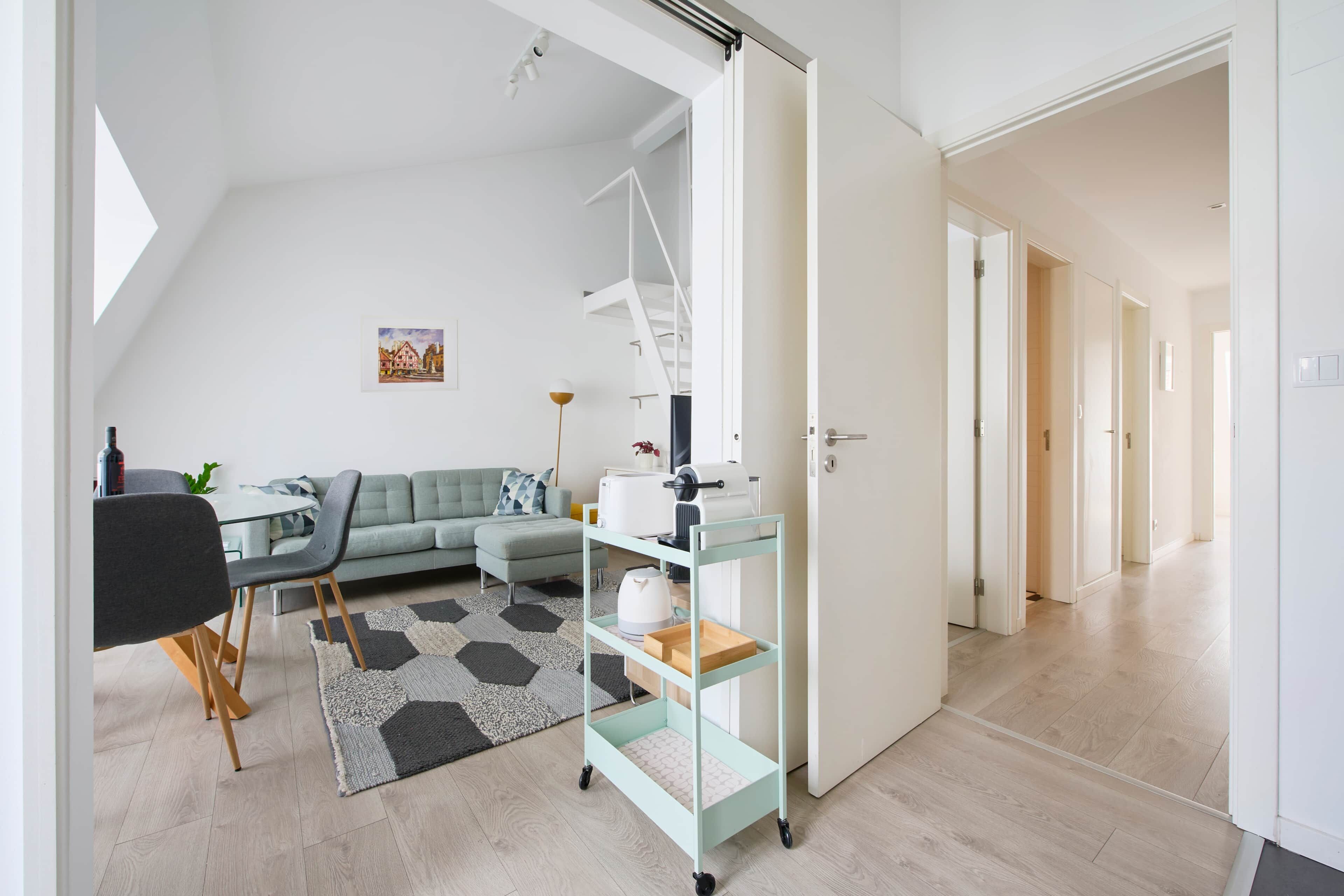 A modern living room with a sofa, a dining table, and a kitchen area with a cart.