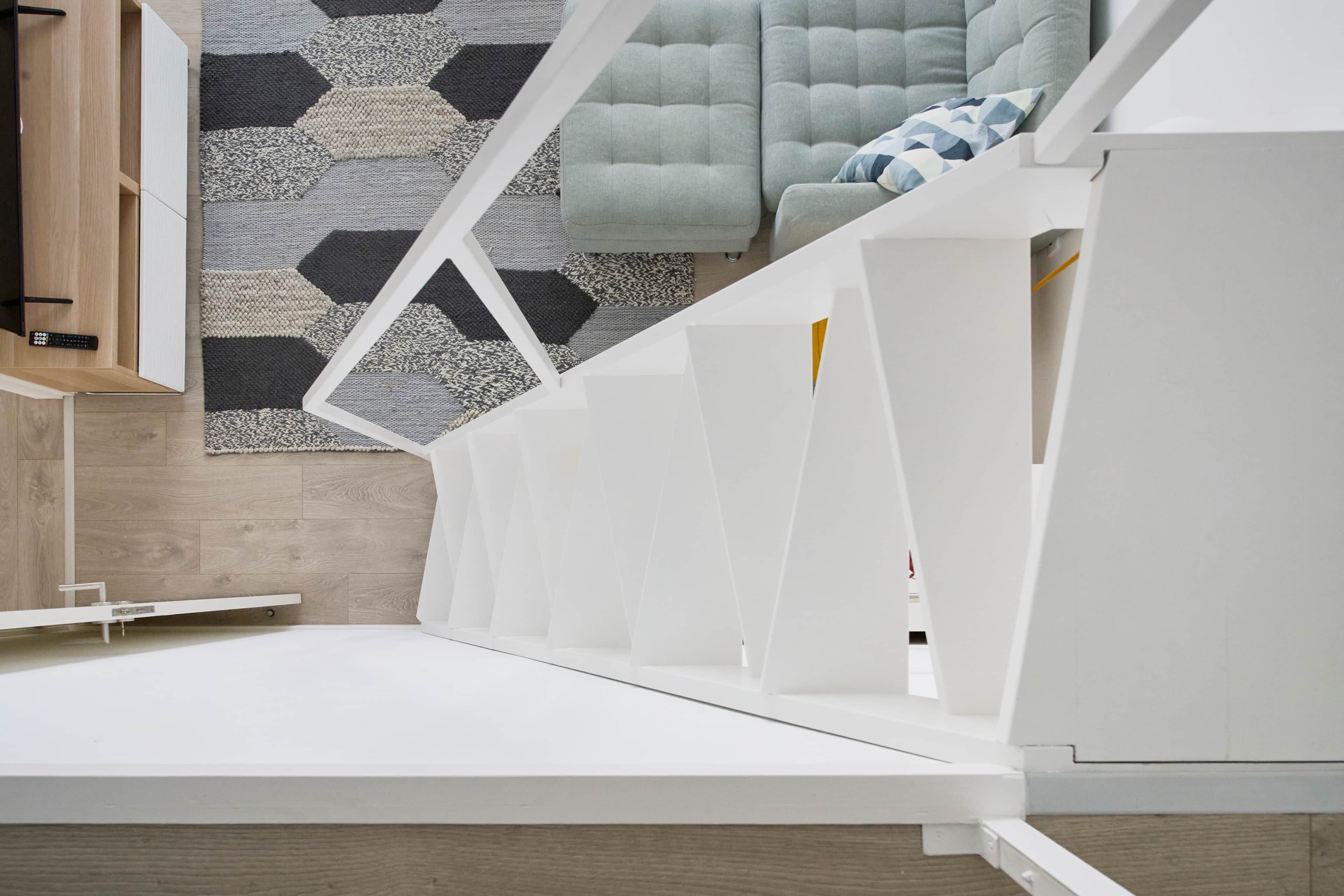 A modern, minimalist room with a white bed frame, a geometric-patterned rug, and a light-colored sofa.