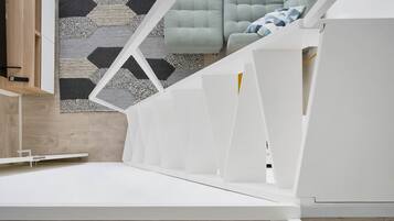 A modern, minimalist room with a white bed frame, a geometric-patterned rug, and a light-colored sofa.