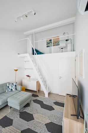 A modern living space with a staircase leading to a loft area, a sofa, a coffee table, and a TV. - NEW! Rooftop Charm Lisbon Retreat (Lisbon)