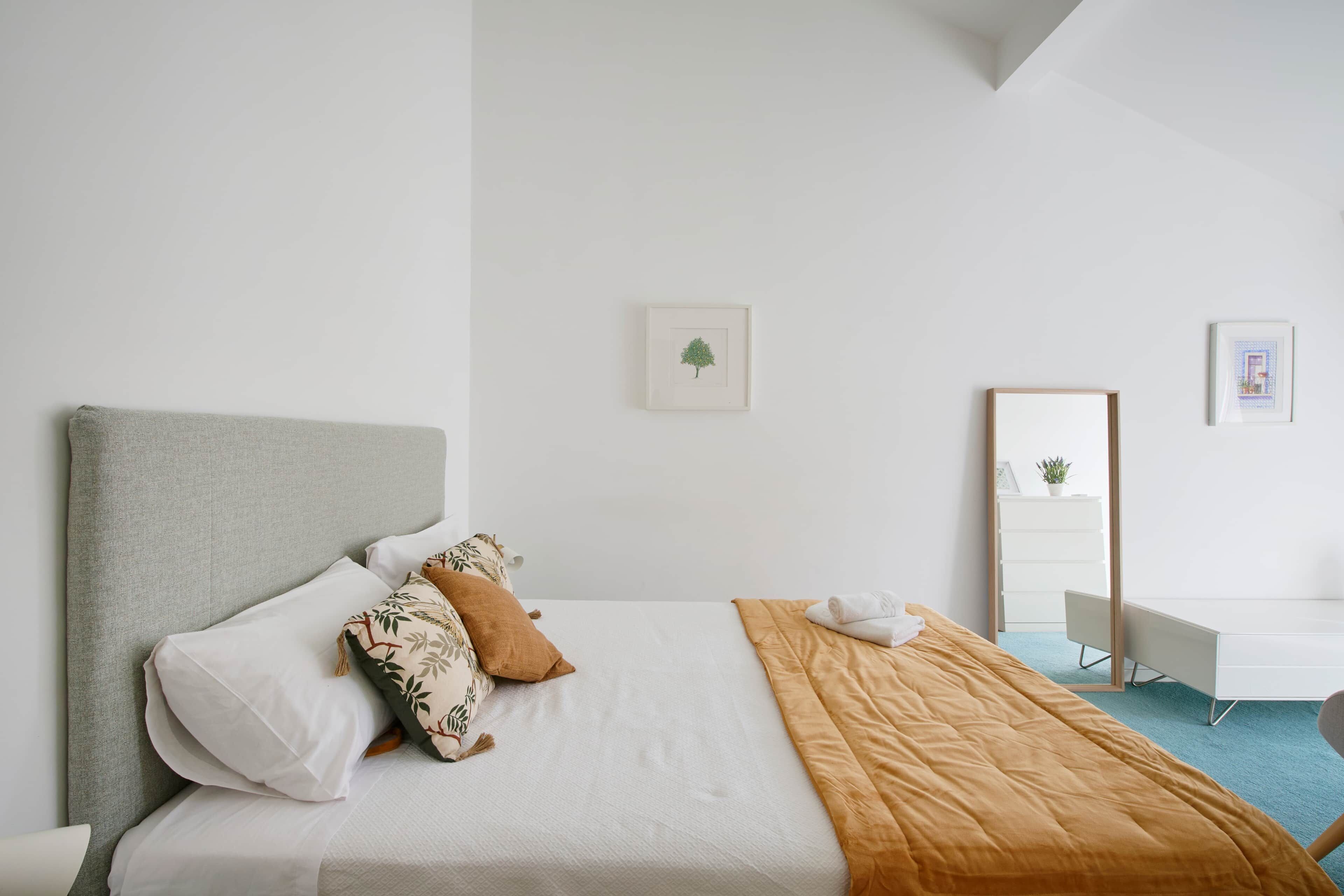 A modern hotel room with a bed, a desk, and a mirror.
