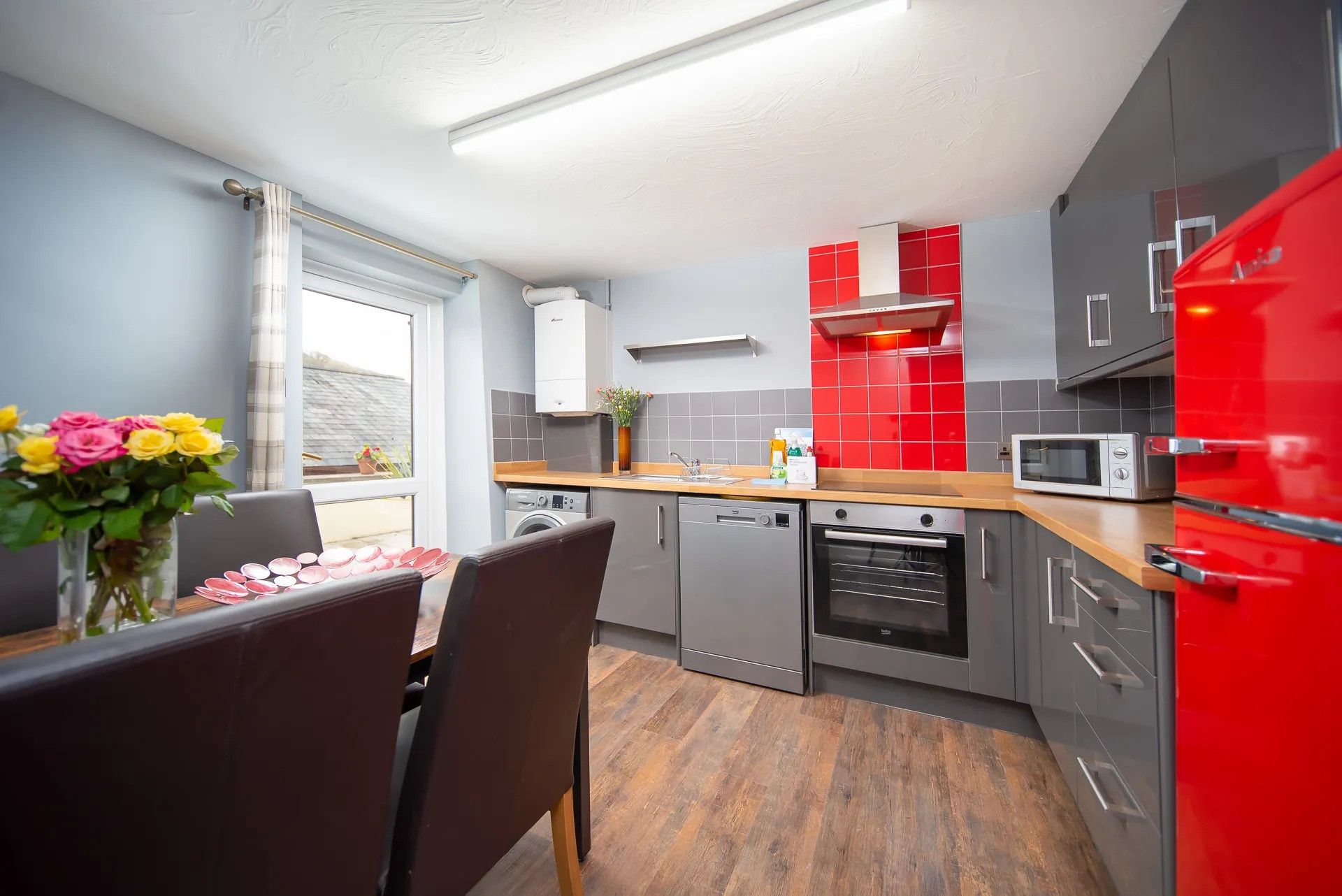Una cocina moderna con armarios grises, un refrigerador rojo y una encimera de madera.