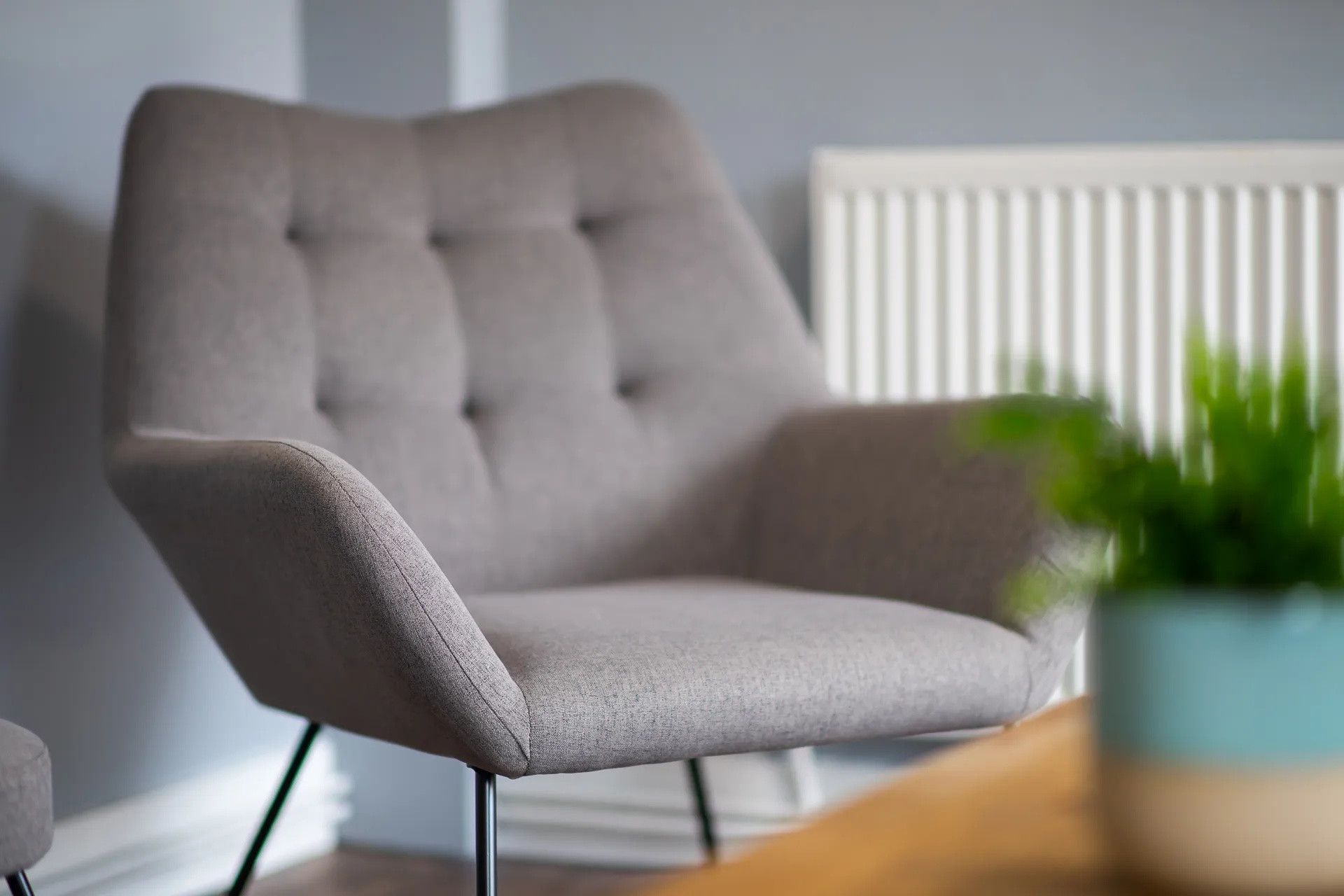 A modern armchair with a tufted backrest and metal legs, positioned in a room with a radiator and a potted plant.