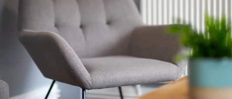 A modern armchair with a tufted backrest and metal legs, positioned in a room with a radiator and a potted plant.