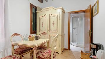 A dining area with a table and chairs, a cabinet, a shower, and a coffee machine.