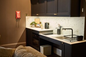 Una cocina compacta con muebles oscuros, encimera de mármol y un lavamanos integrado.