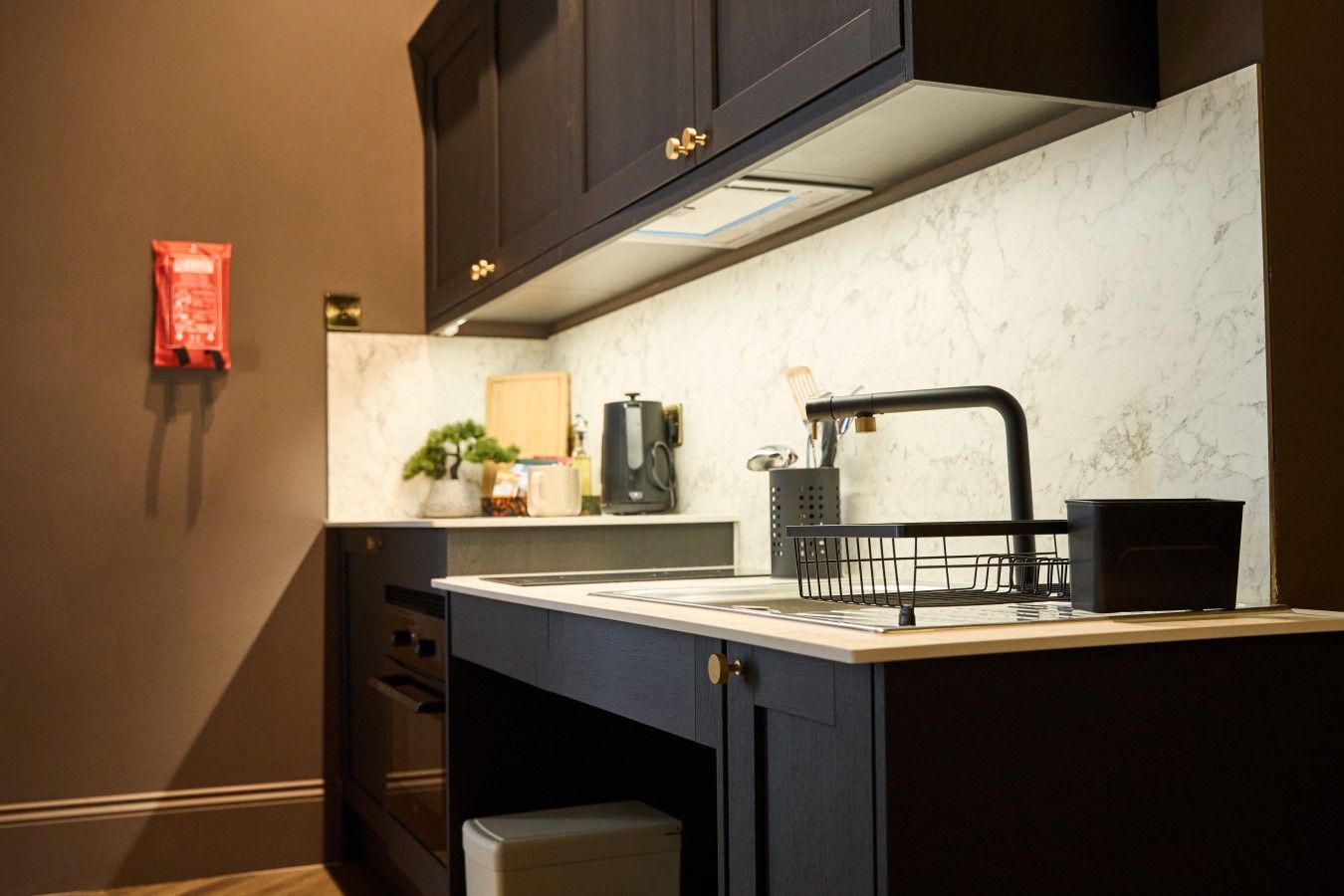 A kitchen with dark cabinets, a marble backsplash, a coffee maker, and a black sink with a faucet.
