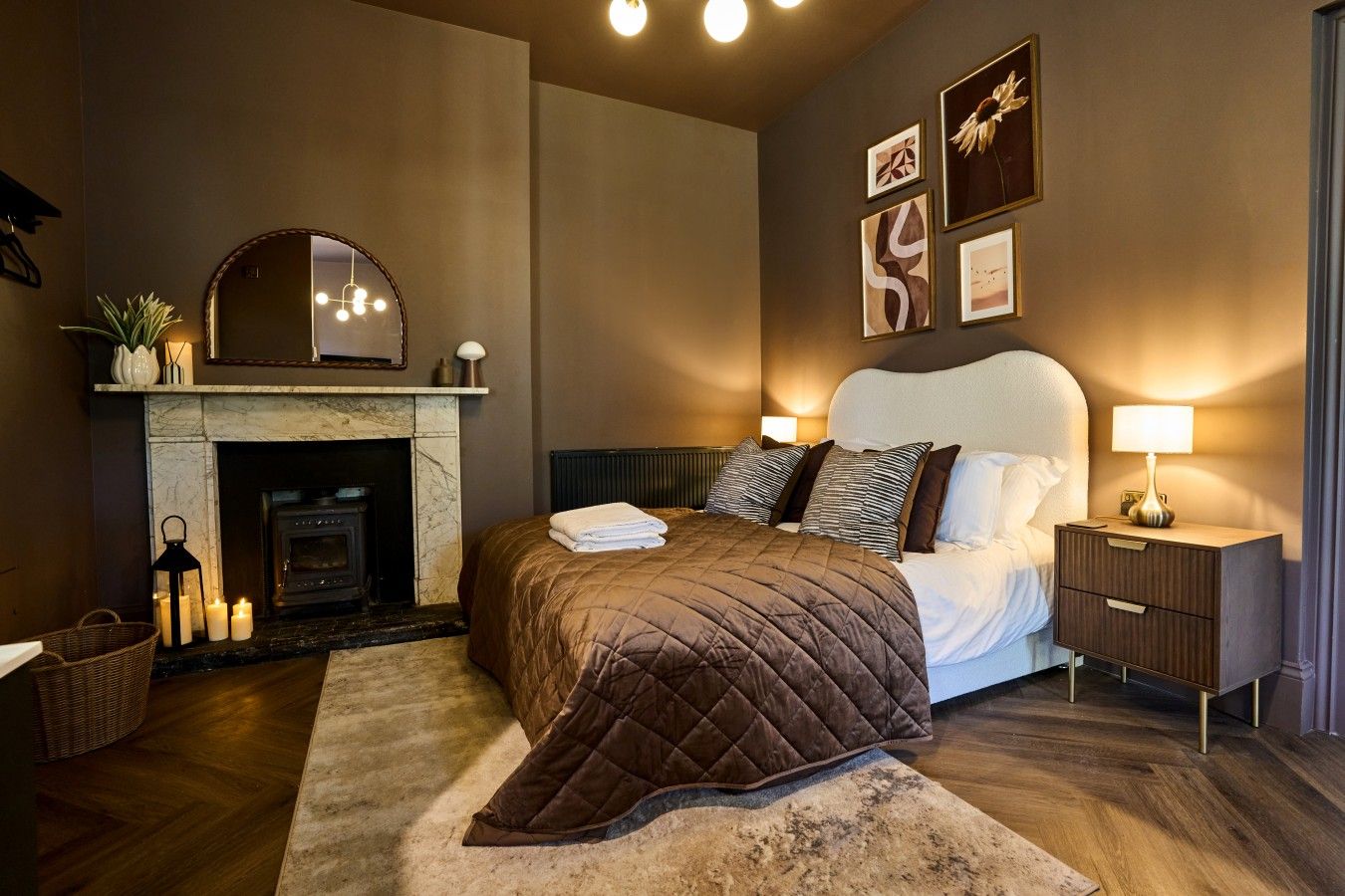 A bedroom with a fireplace, a bed with a quilted bedspread, bedside lamps, and framed artwork on the wall.