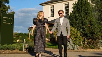 A couple holding hands in front of a building with a sign indicating rooms 1-16 and a house named Sussex House.