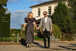 A couple holding hands in front of a building with a sign indicating rooms 1-16 and a house named Sussex House. - *NEW* Large Luxury Garden Terrace Suite in South Downs (Warningcamp)
