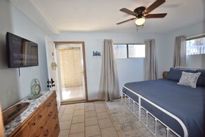 Une chambre à coucher comprenant un lit, un ventilateur de plafond, un téléviseur, une commode et une porte donnant sur un balcon.