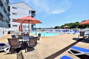 Un espace aménagé au bord de la piscine, avec des chaises longues, des parasols et un bâtiment sur lequel est apposée une enseigne.