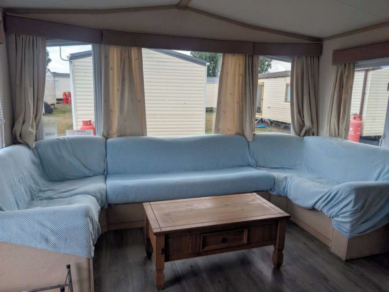 L'intérieur d'une caravane, avec un canapé modulable, une table en bois et des rideaux.