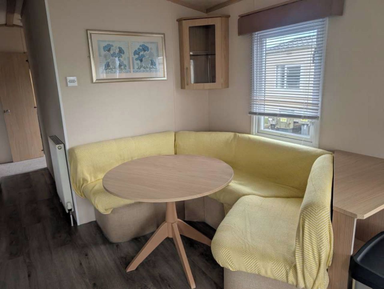 Un espace de vie compact comprenant une table ronde, un banc intégré et une fenêtre avec des stores.
