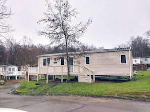 A single-story mobile home with a front deck and a staircase leading to the entrance. - Bluebell corner - with small enclosed decking (Hastings)