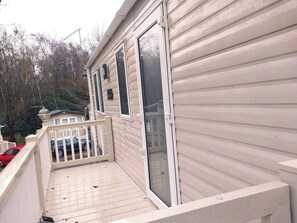 A single-story mobile home with a balcony, a sliding glass door, and a mailbox. - Bluebell corner - with small enclosed decking (Hastings)