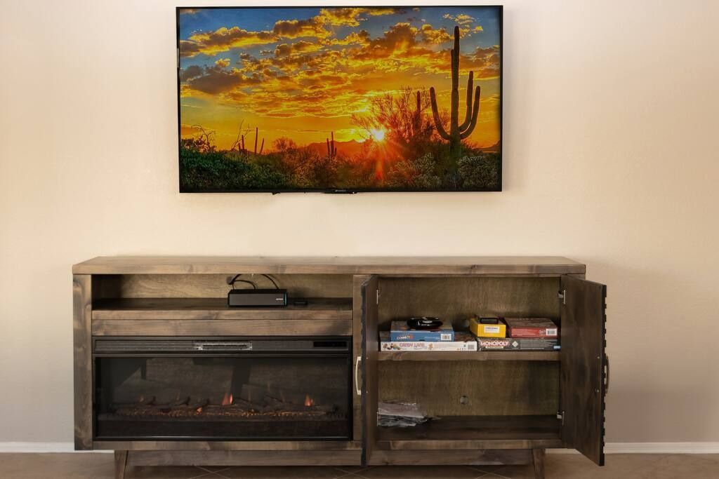 A wooden entertainment center with a flat-screen TV above it, a fireplace below, and a shelf with board games.