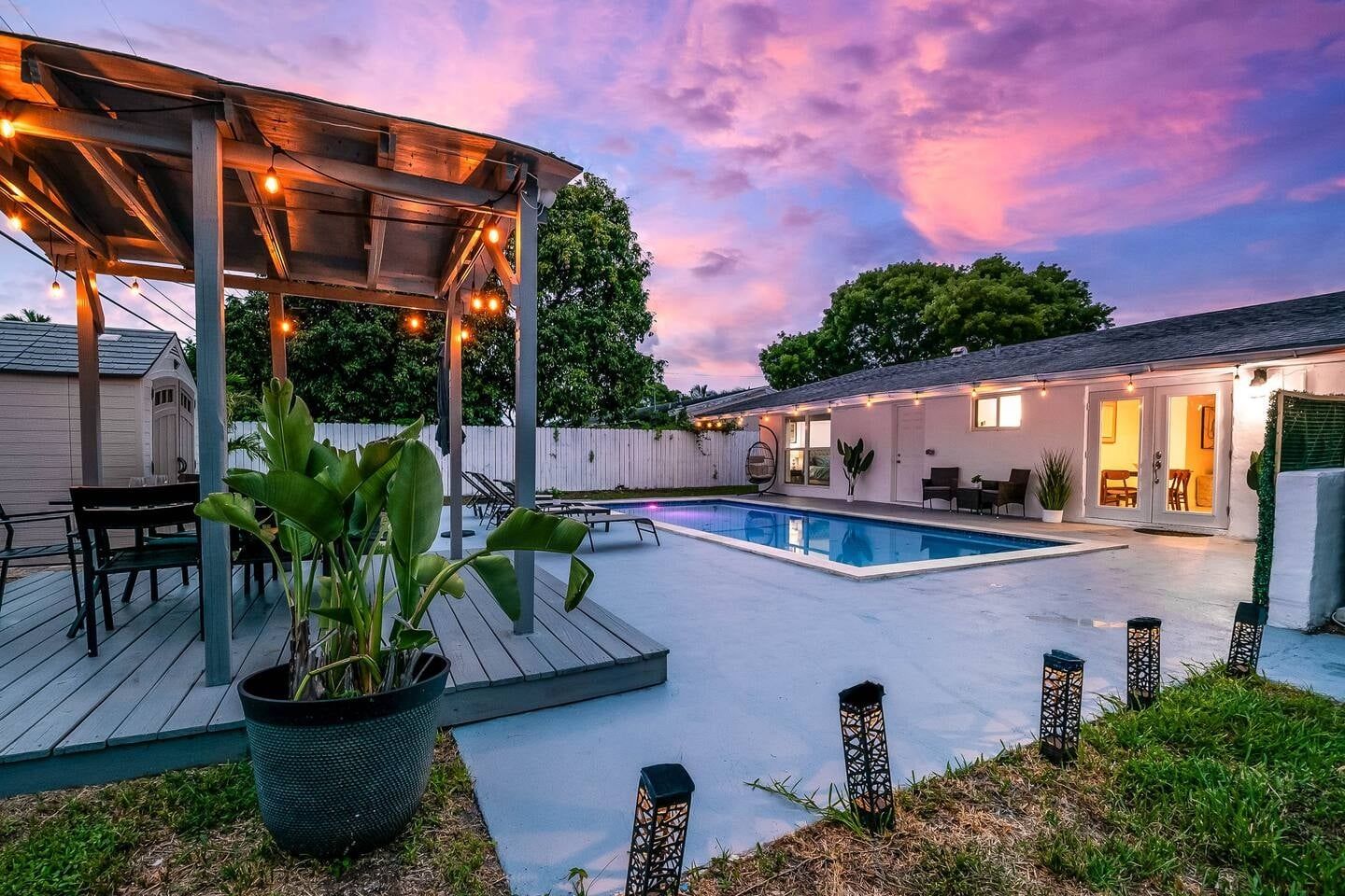 A backyard with a pool, a covered seating area, and a house with a patio.