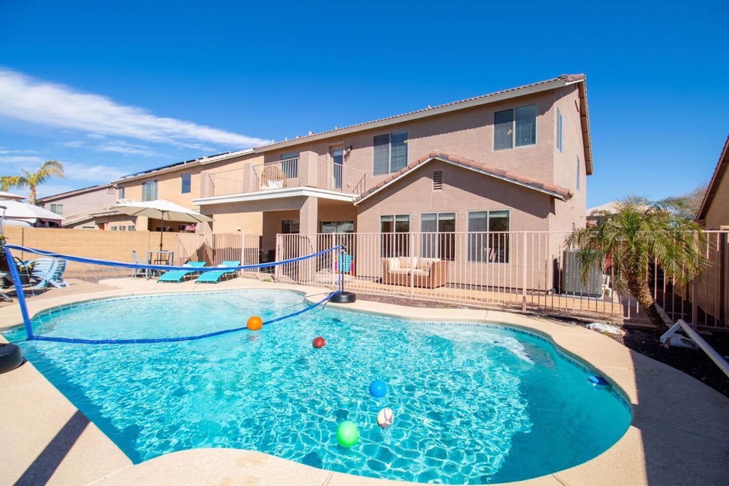 A swimming pool with a blue fence, lounge chairs, and a building with balconies.
