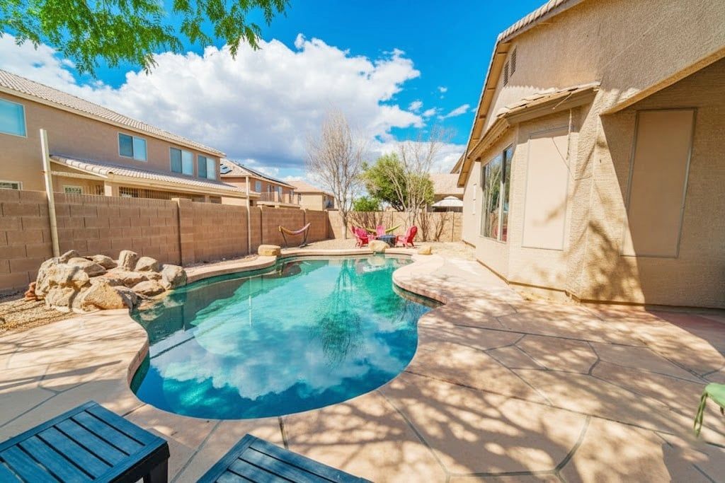 A residential backyard with a swimming pool, patio furniture, and a brick wall.