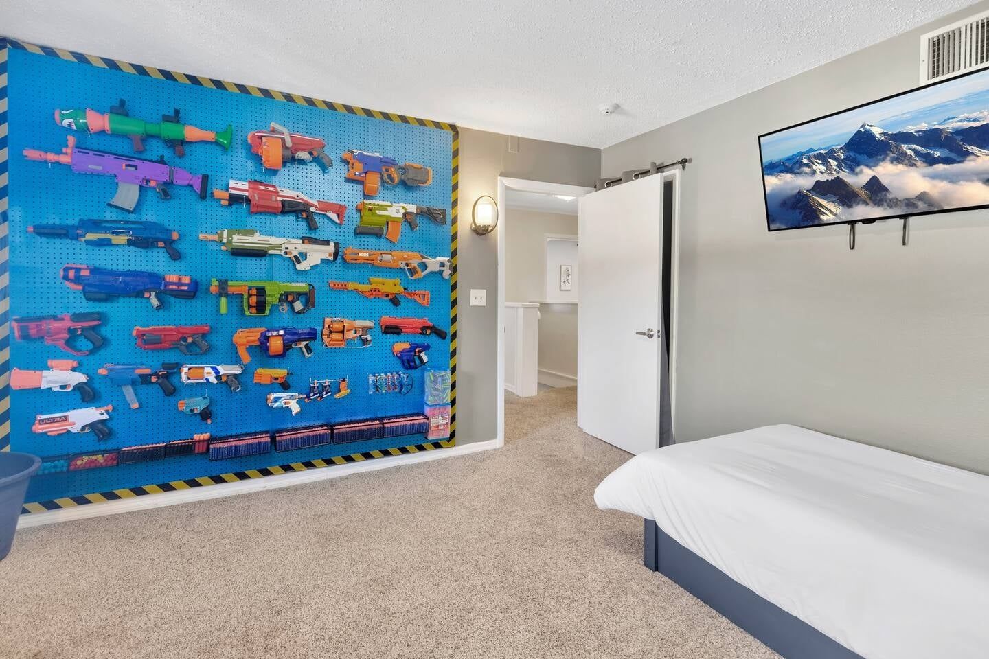 Un dormitorio con una cama, un televisor de pared y un tablón de anuncios con pistolas de juguete.