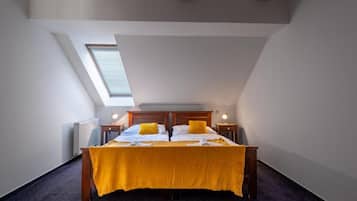 Un dormitorio con techo inclinado, un tragaluz, una cama con colcha amarilla, dos mesitas de noche con lámparas y un radiador.