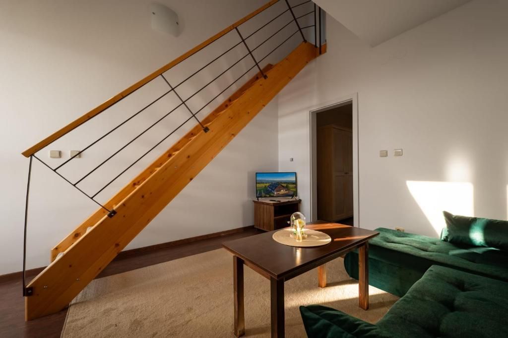Una sala de estar con escalera de madera, un televisor, una mesa con un objeto de vidrio y un sofá verde.