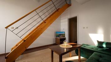 A living room with a wooden staircase, a television, a table with a glass object, and a green sofa.
