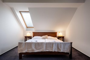 Une chambre avec un plafond en pente, un puits de lumière, un lit en bois, deux tables de chevet avec des lampes et une couvre-lit à motifs.
