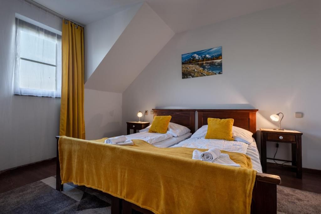 Un dormitorio con una cama, dos mesitas de noche, una ventana con cortinas, un cuadro en la pared y una lámpara sobre las mesitas de noche.