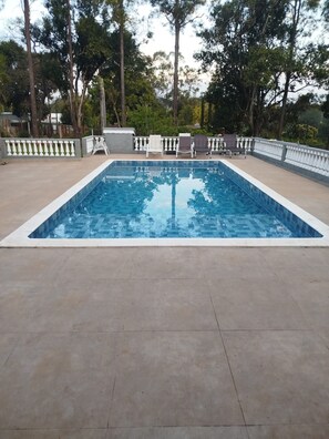 Una piscina rectangular amb vora enrajolada, envoltada per un solàrium de formigó. Hi ha gandules i una taula petita al solàrium.