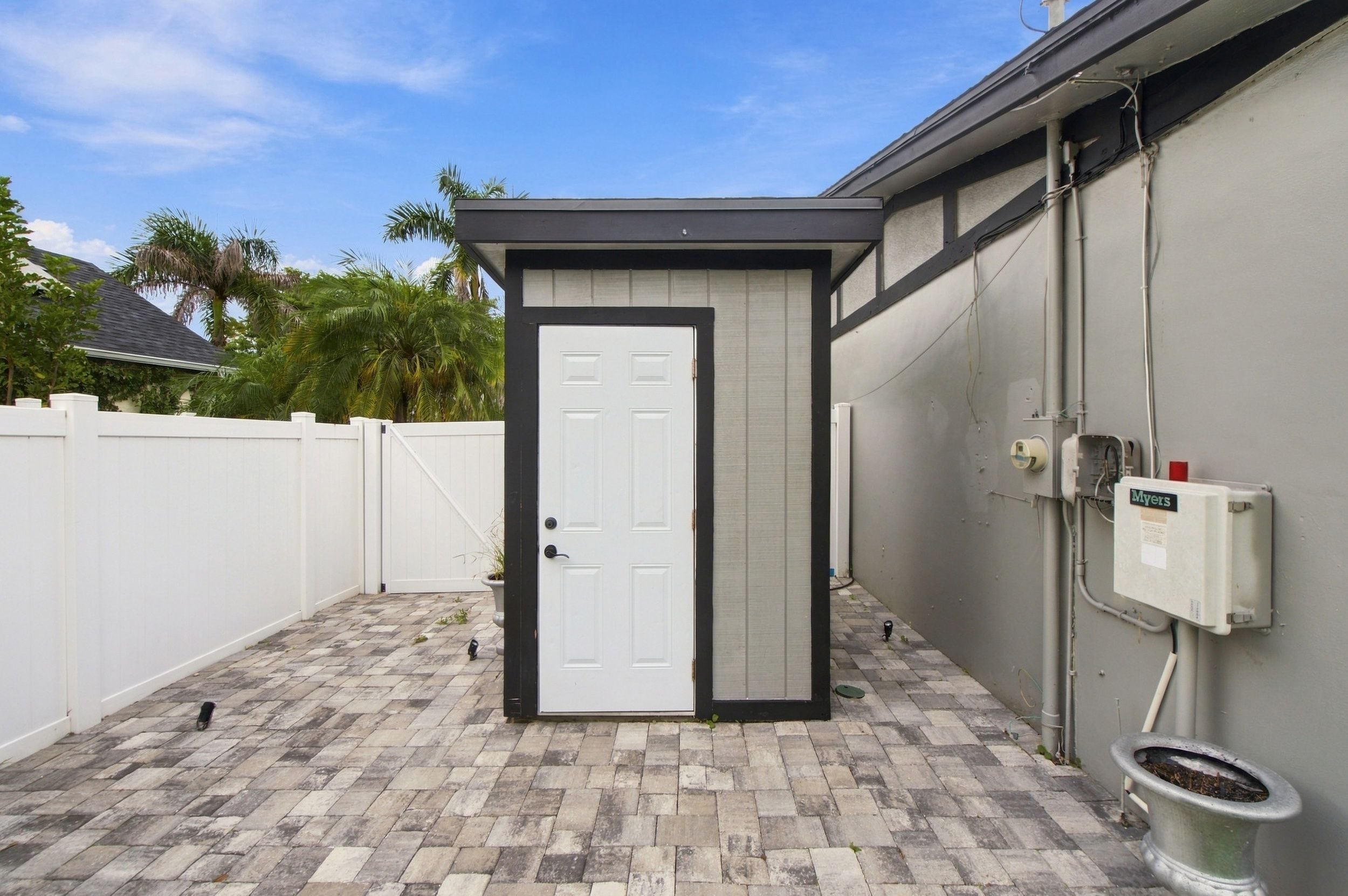 A small, enclosed outdoor area with a white door, a grey wall, and a white fence.