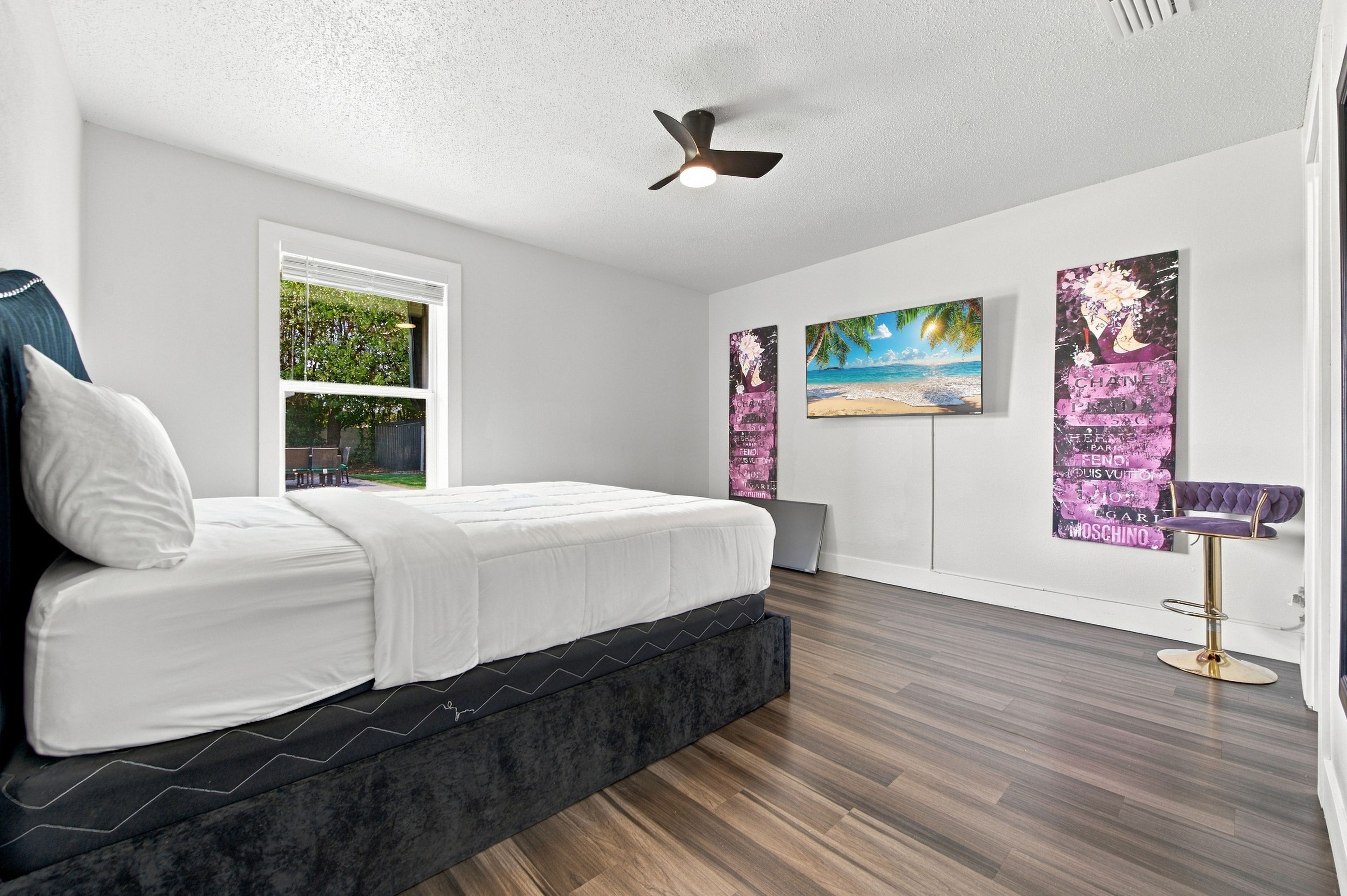 A bedroom with a bed, a ceiling fan, a window, and artwork on the walls.