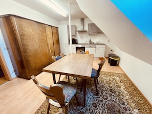 Ein Essbereich mit Holztisch und Stühlen, einem gemusterten Teppich und einer Küche im Hintergrund.