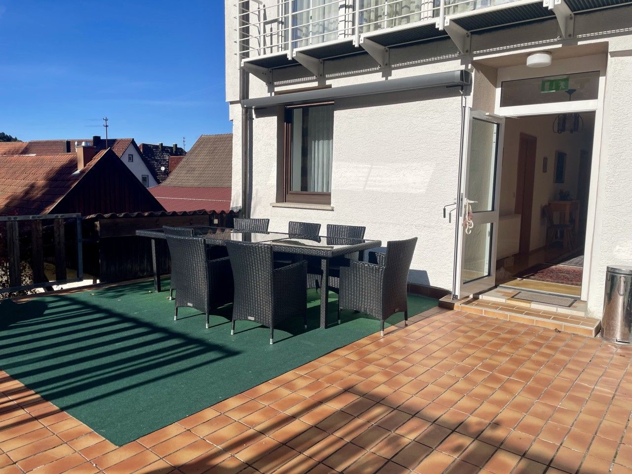 Eine Außenpatio mit Tisch und Stühlen, einer Fläche mit künstlichem Rasen und einem Hauseingang.