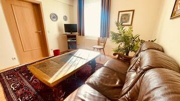 Un salon avec un canapé en cuir marron, une table basse en verre, un téléviseur et une plante en pot.
