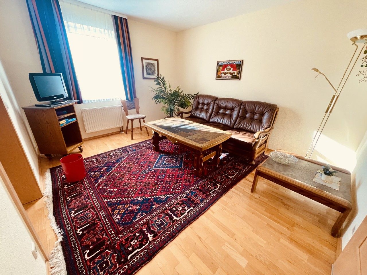 Ein Wohnzimmer mit einer Couch, einem Couchtisch, einem roten Teppich, einem Fernseher und einer Heizung.